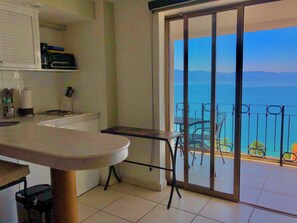 A kitchen with a dining area, a sliding glass door leading to a balcony with a view of the sea. - New Listing (Puerto Vallarta)