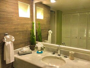 A bathroom with a wooden wall, a sink with a mirror, a towel rack, a potted plant, and a toilet paper holder. - New Listing (Puerto Vallarta)