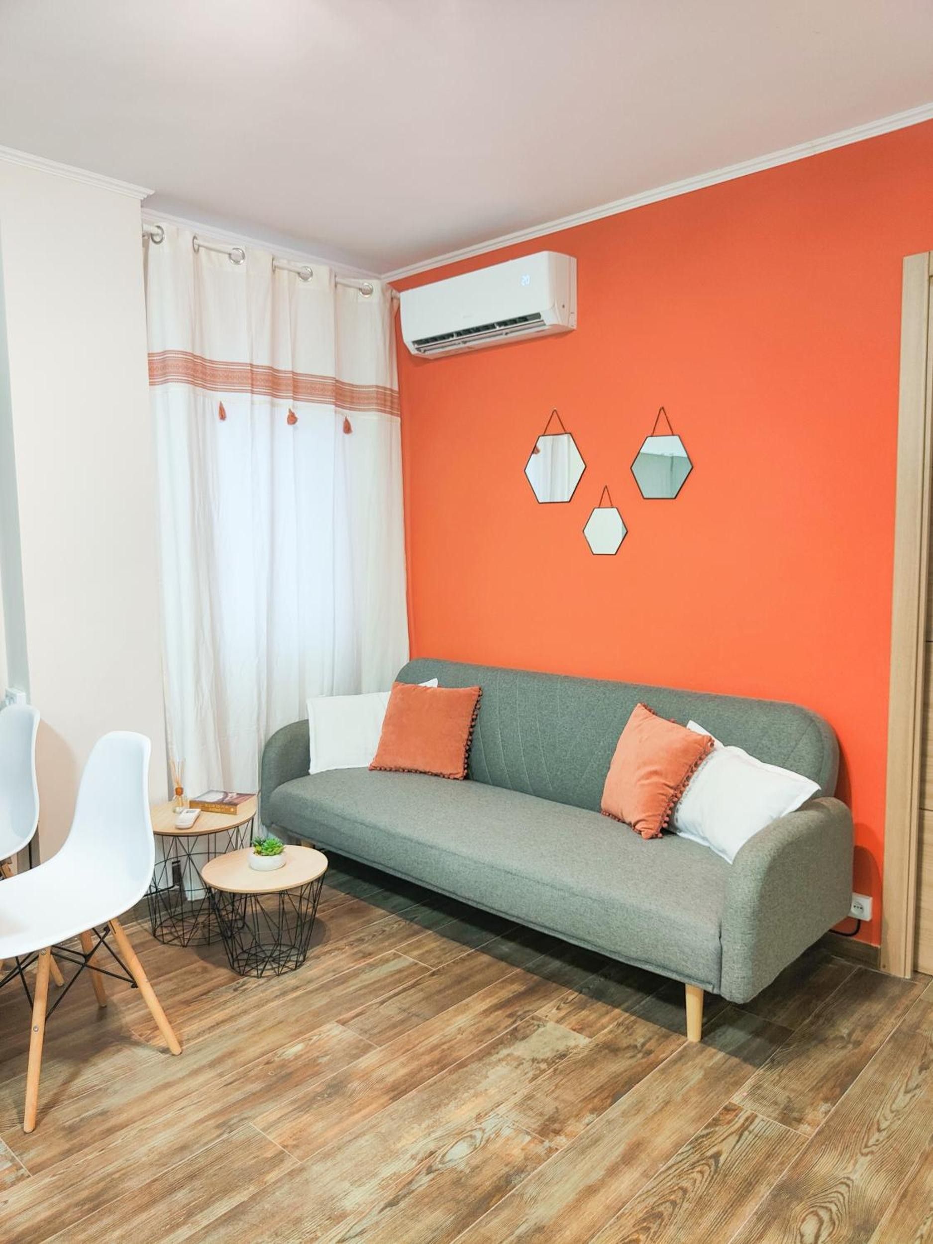 Un salon avec un canapé gris, des chaises blanches, une petite table ronde et un plancher en bois.