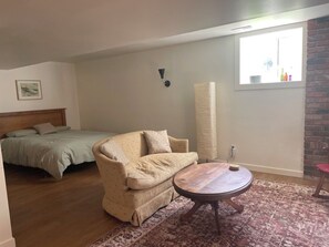 Une chambre avec un lit, un canapé, une table ronde, un tapis, une lampe fixée au mur et une fenêtre donnant sur un beau paysage.