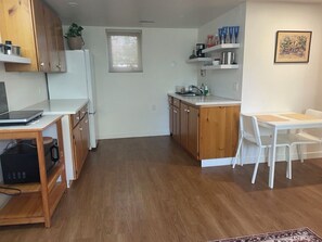 Une cuisine compacte avec des meubles en bois, un réfrigérateur blanc et un coin repas avec des chaises blanches.