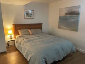 Une chambre à coucher avec un lit, une table de chevet avec une lampe, un tableau encadré au-dessus du lit et une grande peinture au mur.