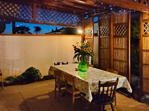 Una terrazza esterna con tavolo e sedie, un vaso con fiori e un recinto in legno con pannelli a griglia.
