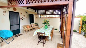 Un'area patio coperta con tavolo e sedie, una sedia blu e una struttura in legno a pergola.
