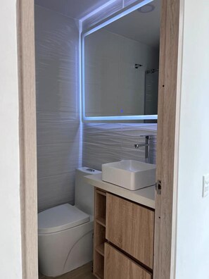 A small, compact bathroom with a toilet, a sink, and a mirror. - Premium Loft La Candelaria (Bogotá)