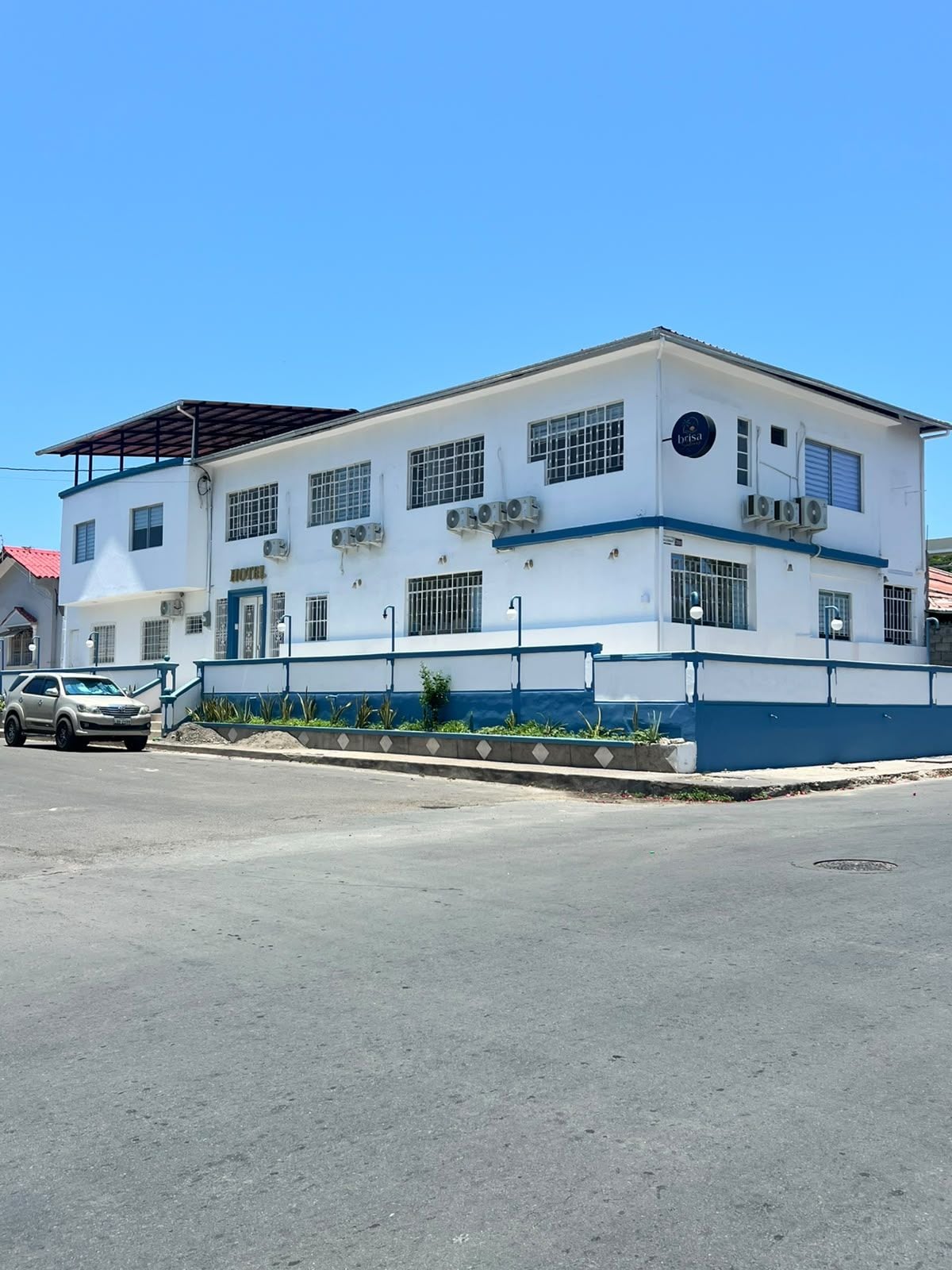 A two-story hotel with a flat roof, multiple air conditioning units, and a gated entrance.