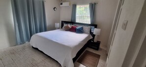 Une chambre à coucher avec un lit, des lampes de chevet, une fenêtre avec des rideaux et un appareil de climatisation.