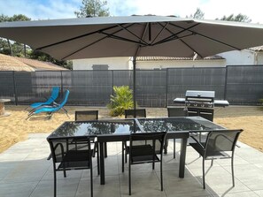 Une terrasse extérieure avec une table et des chaises, un barbecue et un grand parasol.