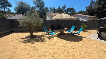 A backyard with a sandy area, a tree, and blue lounge chairs.