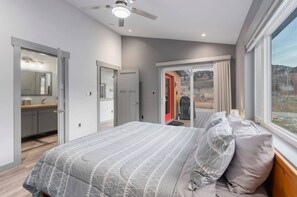 Un dormitorio con cama, ventilador de techo, ventana con vistas y baño con espejo y lavamanos.