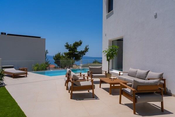 A modern outdoor patio with a pool, lounge chairs, and a view of the sea. - Villa A, modern villa on a peaceful hillside in Podstrana (Podstrana)