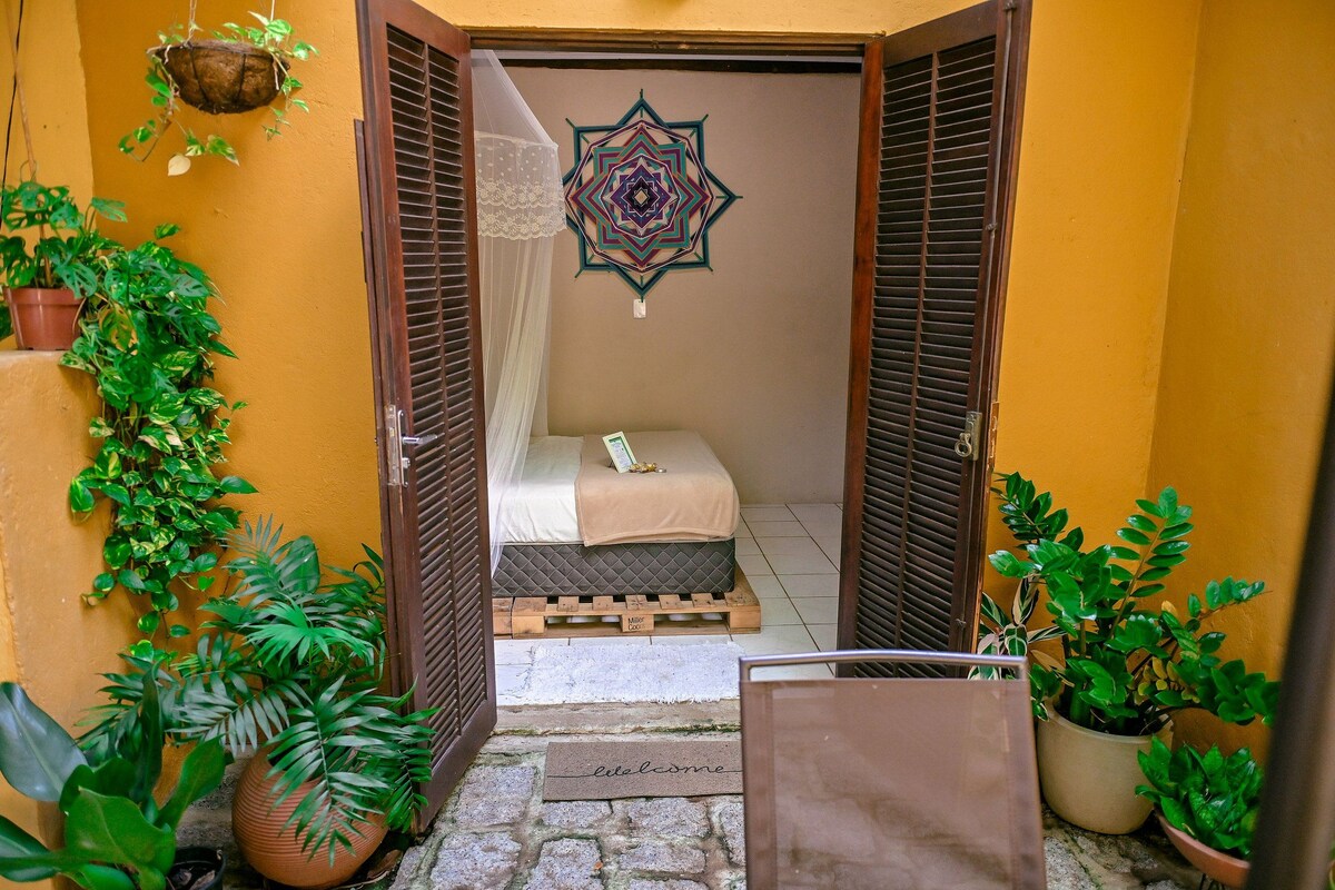 Un pasillo estrecho que conduce a un dormitorio con una cama, felpudo y plantas en macetas.