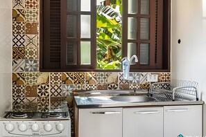 Una cocina con estufa a gas, un lavamanos y un ventanal con contraventanas marrones.