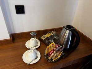 Une table dressée pour le petit-déjeuner avec deux tasses blanches, un verre d’eau, une cafetière et un panier contenant un assortiment de viennoiseries.