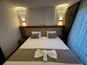 Une chambre d’hôtel avec un lit, deux lampes de chevet, une table de nuit et une fenêtre avec des rideaux.