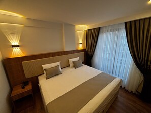 Une chambre d’hôtel avec un grand lit, des lampes de chevet, une tête de lit en bois, une table de chevet et une fenêtre avec des rideaux.
