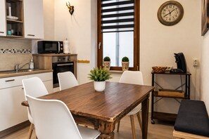 Eine kleine Küche mit Holztisch, weißen Stühlen, einer Mikrowelle und einer Kaffeemaschine.