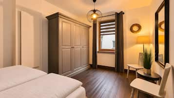 Ein Schlafzimmer mit Bett, Kleiderschrank, Nachttisch, Lampe, Stuhl und einem Fenster mit Vorhängen.