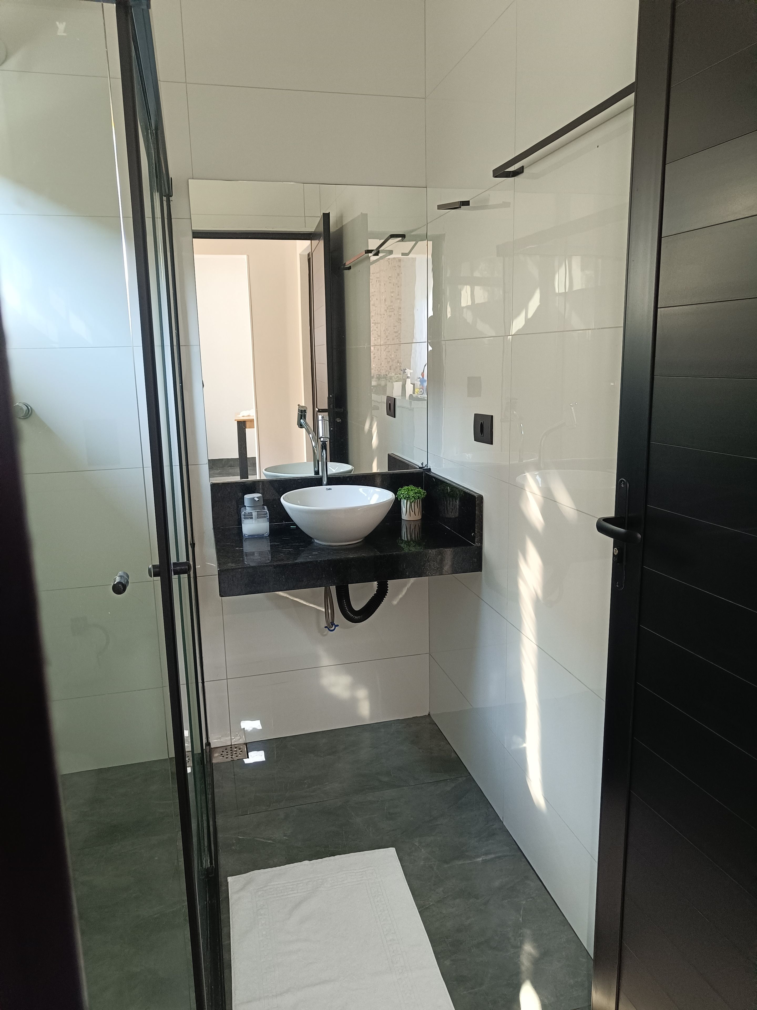 A modern bathroom with a white sink, black countertop, and a glass shower enclosure.