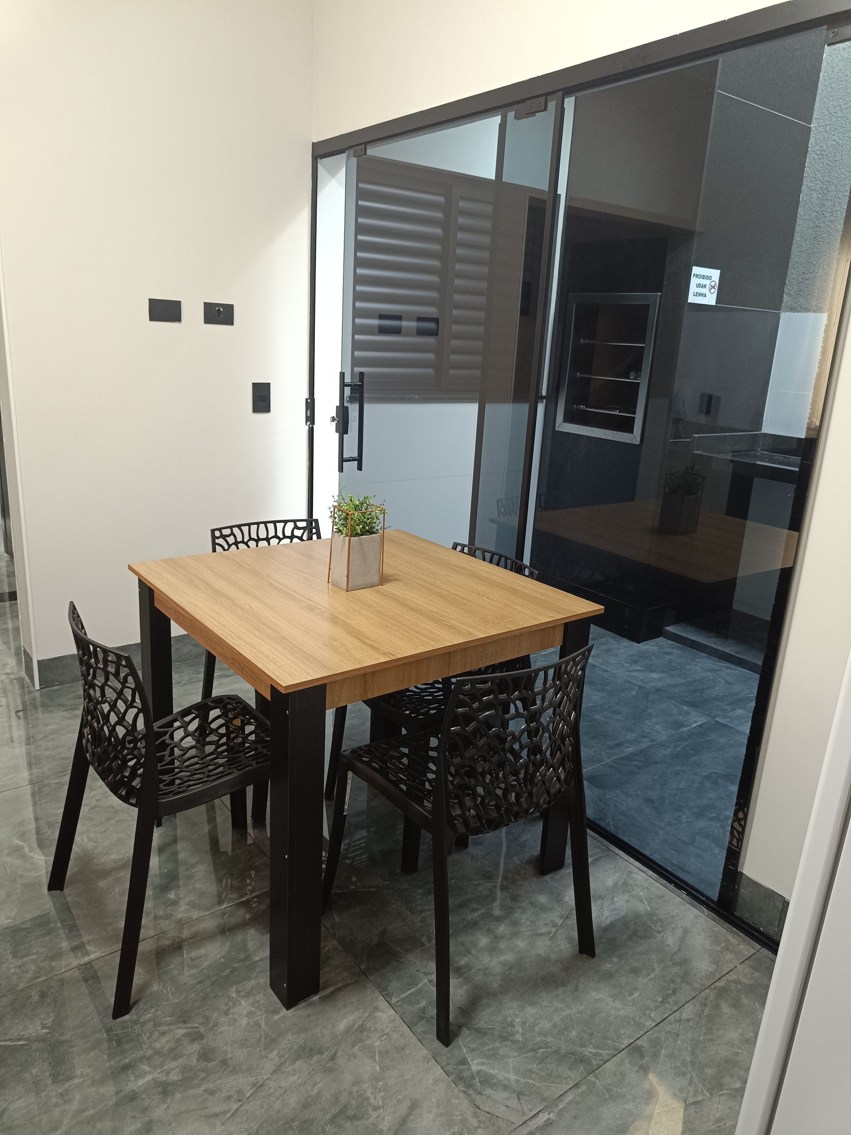 A room with a wooden table and chairs, a potted plant, and a sliding glass door leading to another area.