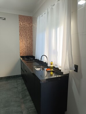 A modern kitchen with a black countertop, stainless steel sink, and a tiled backsplash. - Studio 2 (Porto Rico)