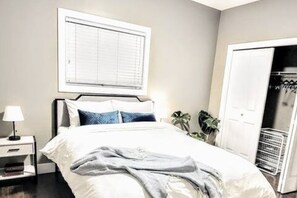 Un dormitorio con una cama, una mesita de noche, una ventana con persianas y una puerta a un armario.