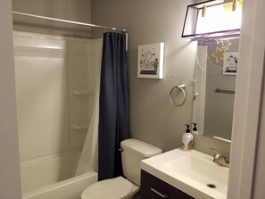 Un baño con ducha, inodoro, lavamanos y un espejo con tozaleta.
