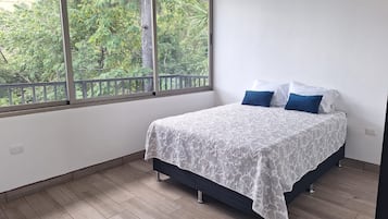 Un dormitorio con cama, ventana y vista a zonas verdes.