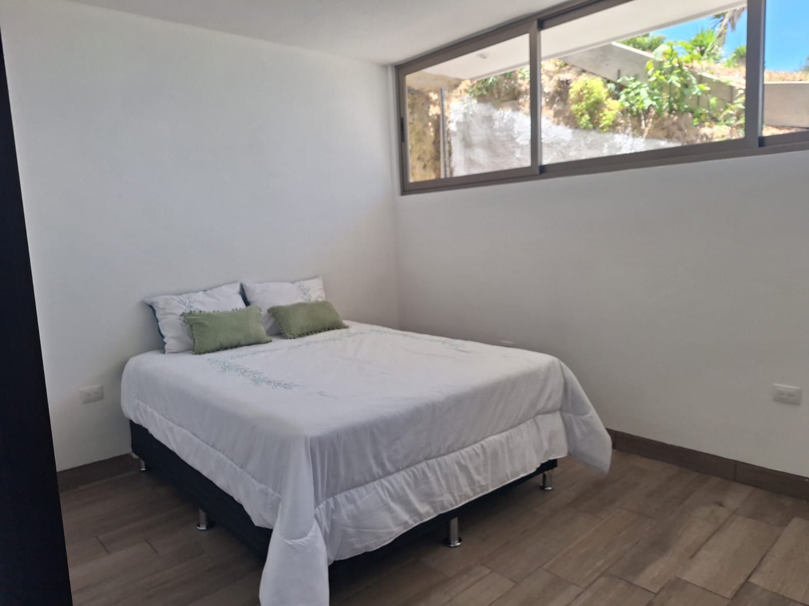 Un dormitorio con cama, ventana y vista a la vegetación.