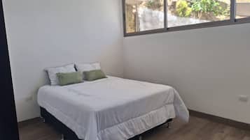 Un dormitorio con cama, ventana y vista a la vegetación.