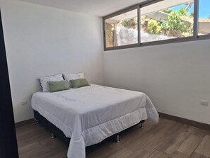 Un dormitorio con cama, ventana y vista a la vegetación.