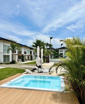Ein Swimmingpool mit Liegestühlen und Sonnenschirmen, umgeben von Palmen und einem Gebäude mit einem Balkon.