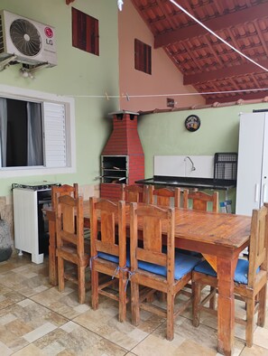 A kitchen with a red brick oven, a white refrigerator, and a dining table with wooden chairs. - New Listing (Mongaguá)