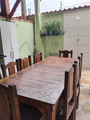A wooden dining table with chairs, a white cabinet, and a green wall with potted plants. - New Listing (Mongaguá)