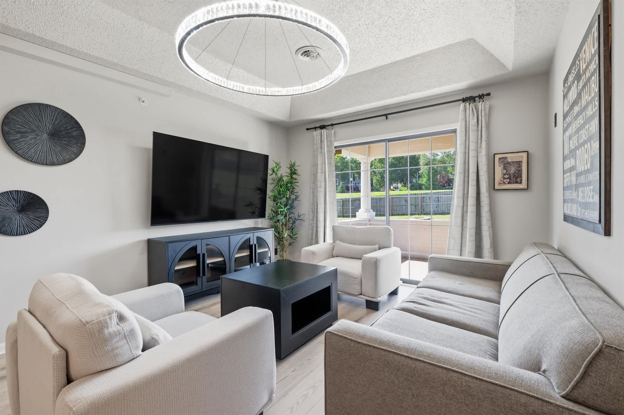 A modern living room with a flat-screen TV, two sofas, a coffee table, and a large window with curtains.