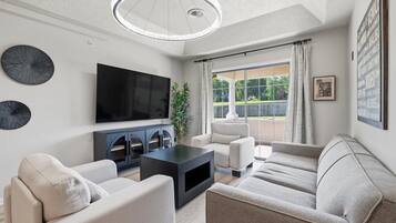 A modern living room with a flat-screen TV, two sofas, a coffee table, and a large window with curtains.
