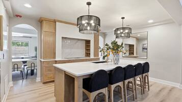 A modern kitchen with a large island, wooden cabinets, and pendant lighting.