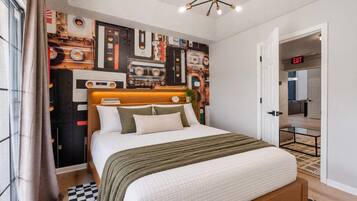 A modern bedroom with a bed, a headboard with a clock, a wall with cassette tapes, and an exit sign.
