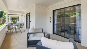 A covered patio area with a dining table and chairs, a sofa, and a sliding glass door leading to a backyard.