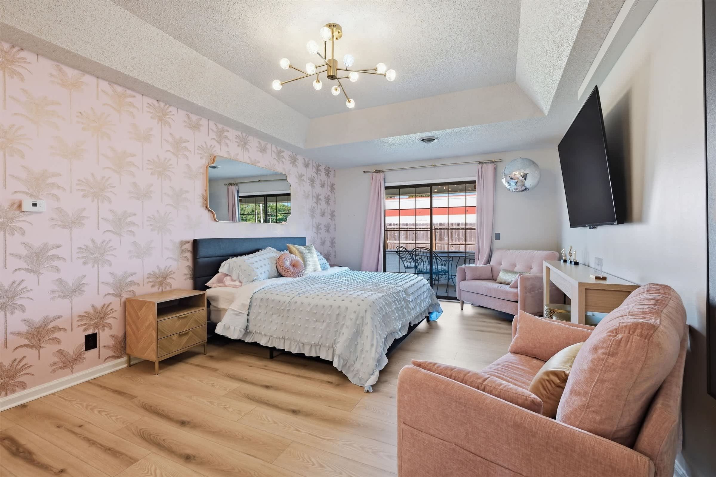 Un dormitorio con cama, cómoda, silla, televisión y balcón con vistas.