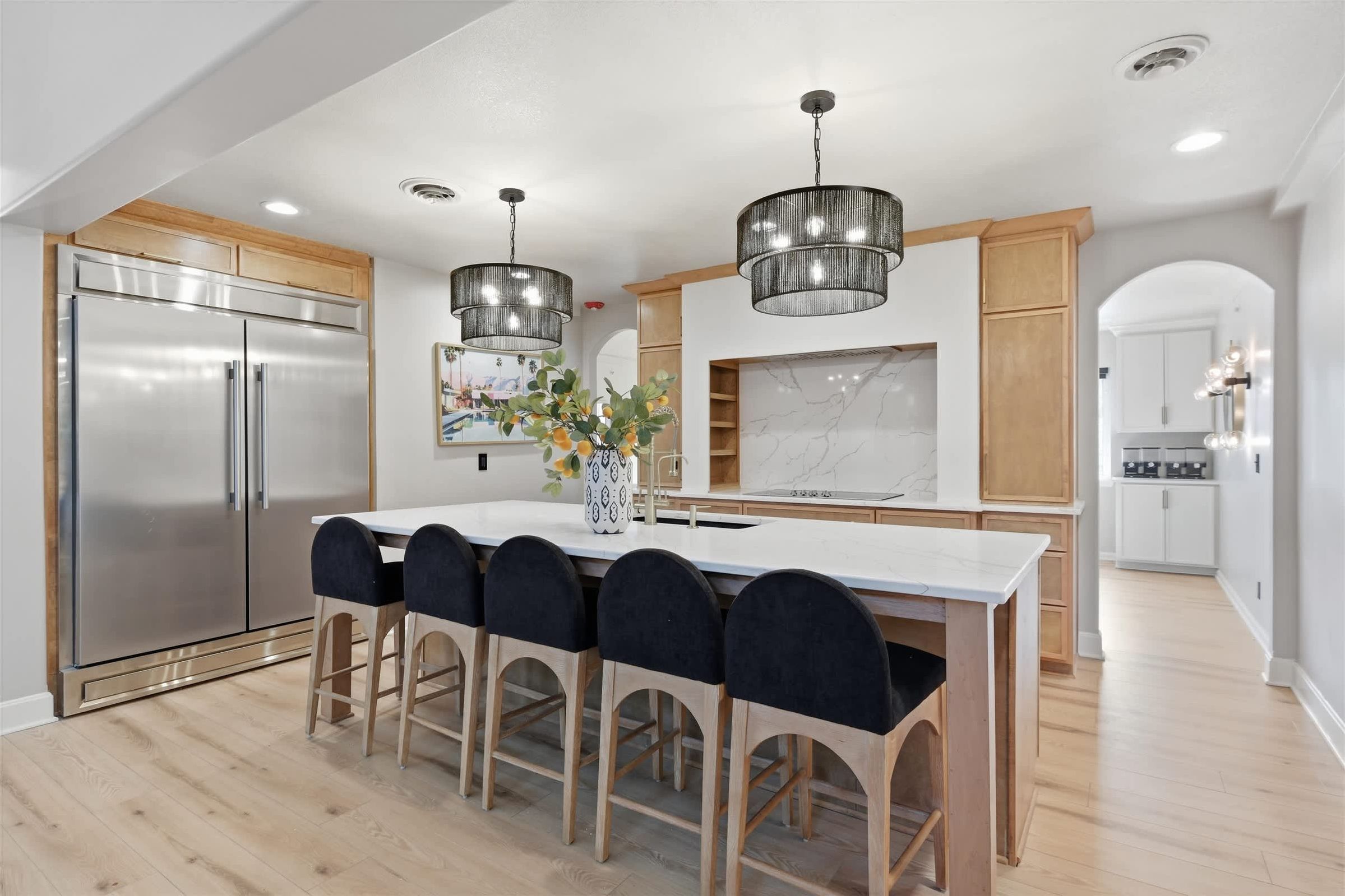 Una cocina moderna con un refrigerador de acero inoxidable, una encimera de mármol y una isla central con taburetes de bar.