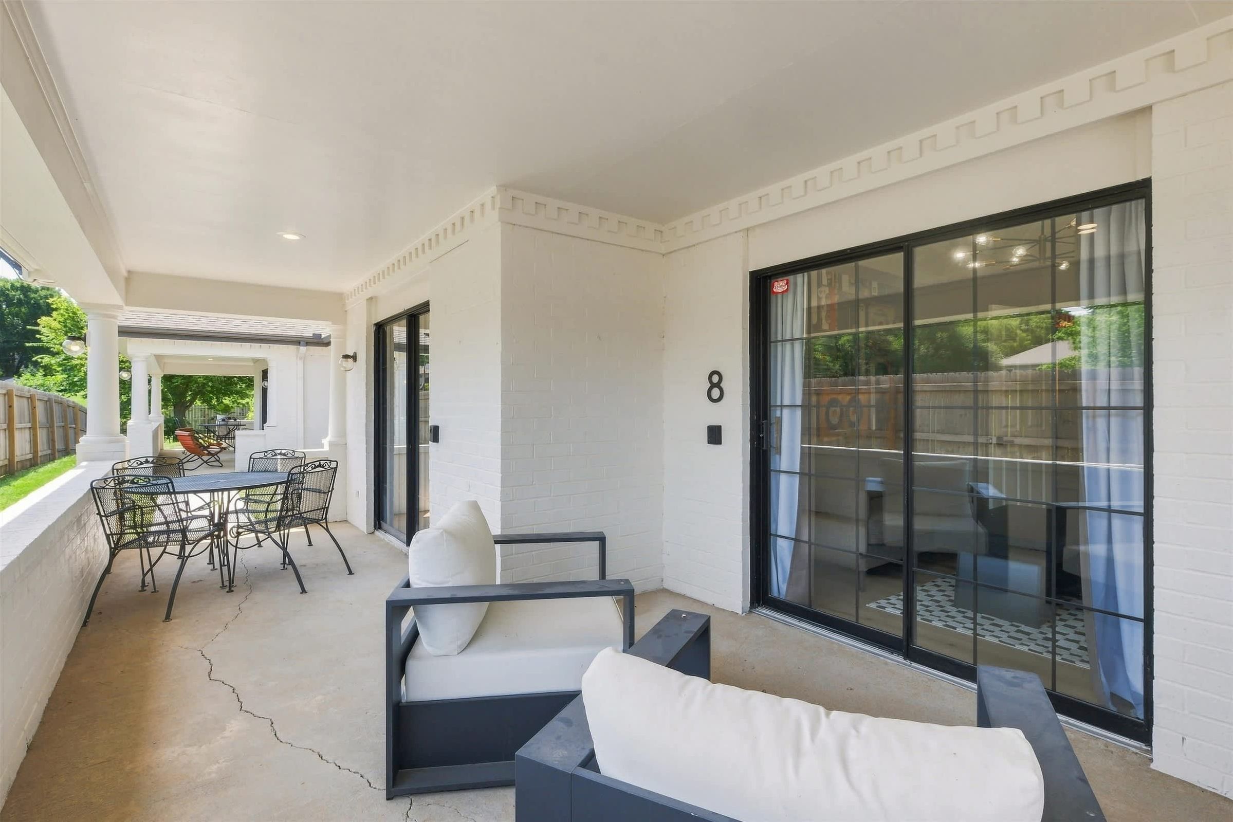 A covered patio area with a dining table and chairs, a sofa, and a sliding glass door leading to a backyard.