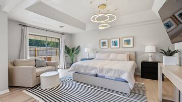 A modern bedroom with a bed, bedside tables, a sofa, a striped rug, and a ceiling light fixture.