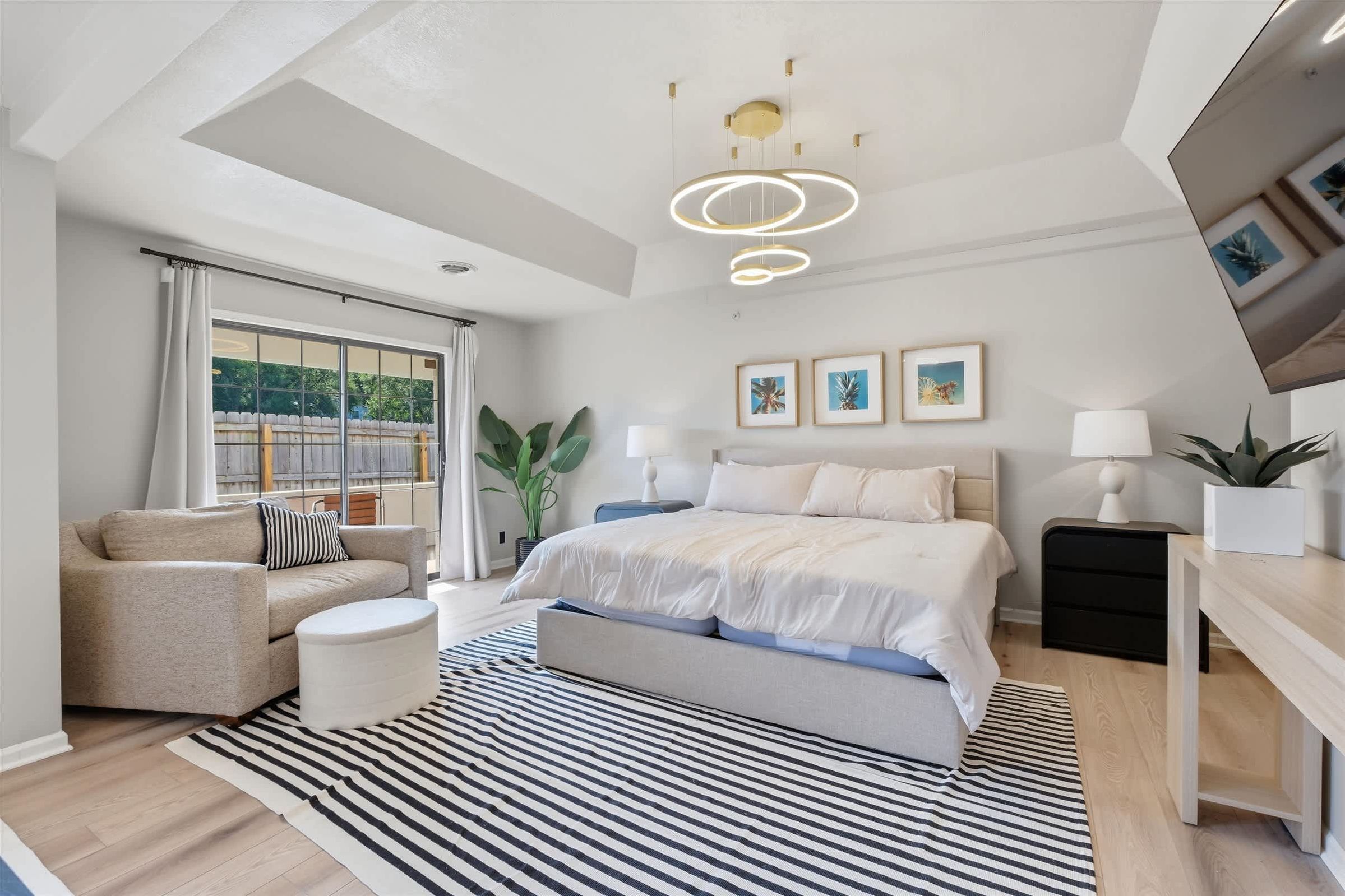 A modern bedroom with a bed, bedside tables, a sofa, a striped rug, and a ceiling light fixture.