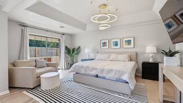 A modern bedroom with a bed, bedside tables, a sofa, a striped rug, and a ceiling light fixture.