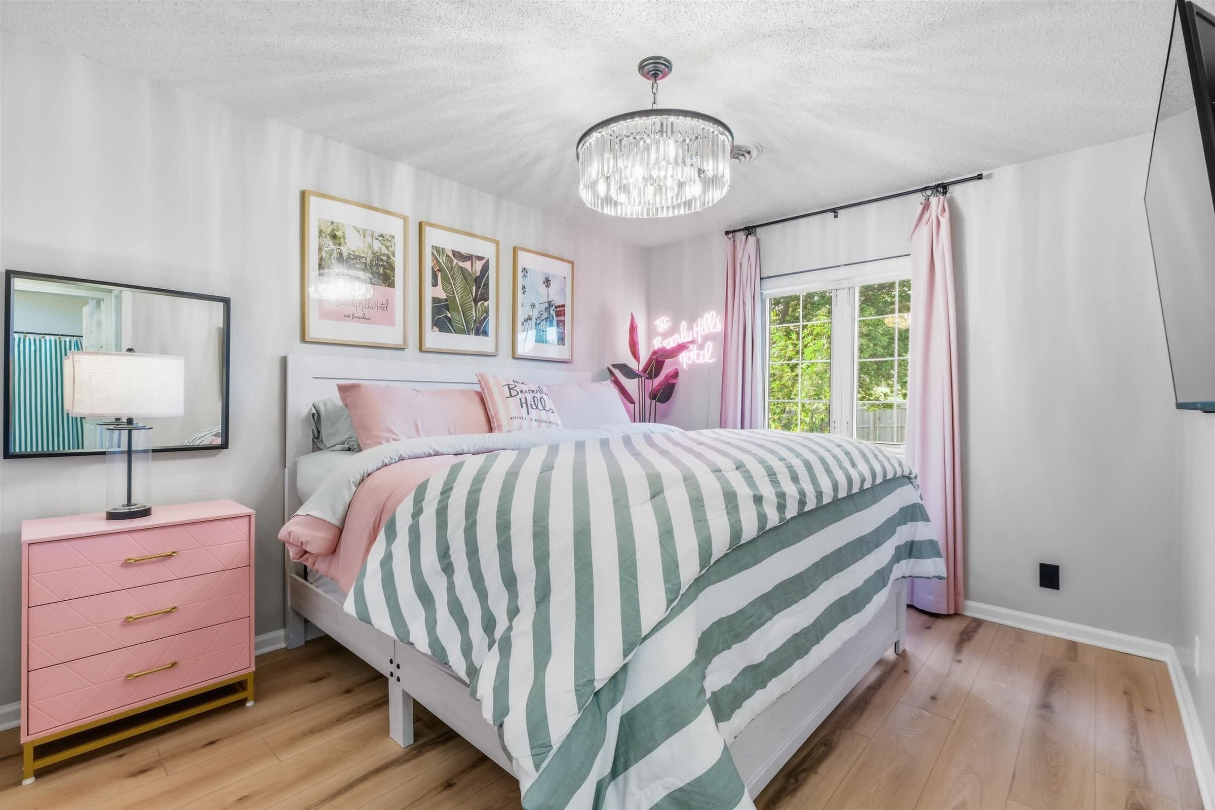 A bedroom with a bed, a nightstand, a dresser, a chandelier, and framed pictures on the wall.