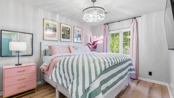 A bedroom with a bed, a nightstand, a dresser, a chandelier, and framed pictures on the wall.