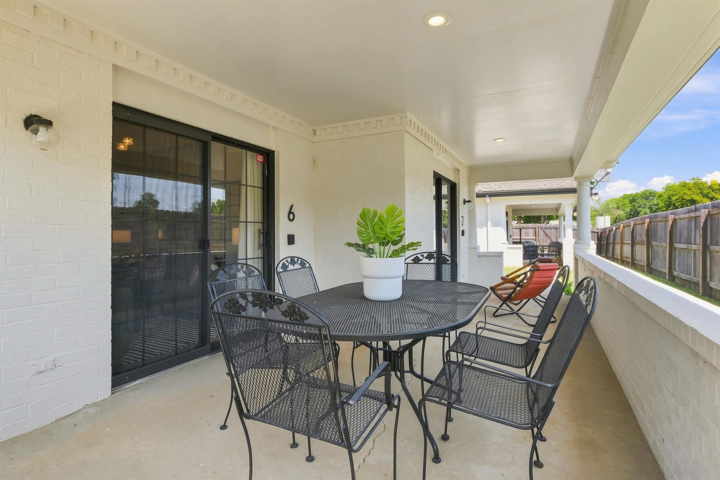 A covered patio with a round table and chairs, a potted plant, and a view of the backyard.