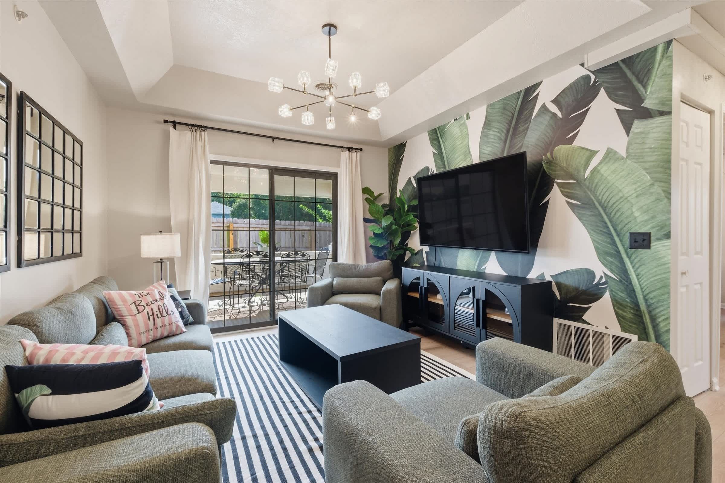 A modern living room with a sofa set, a coffee table, a TV mounted on the wall, and a large window with curtains.
