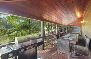 Eine überdachte Terrasse im Freien mit Grill, Korbmöbeln und Blick auf ein bewaldetes Gebiet.